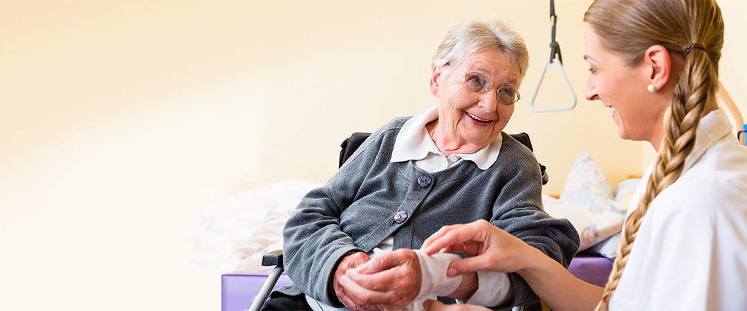 Healthcare worker with long blond braid helping senior woman with wrap around her wrist.